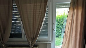 Una stanza con pavimento in legno, termosifone, finestra con persiane e tende.