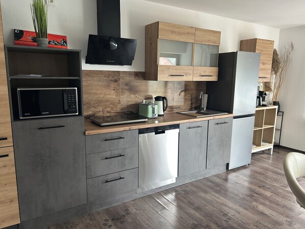 Una cocina moderna con microondas integrado, lavavajillas y cafetera sobre la encimera.