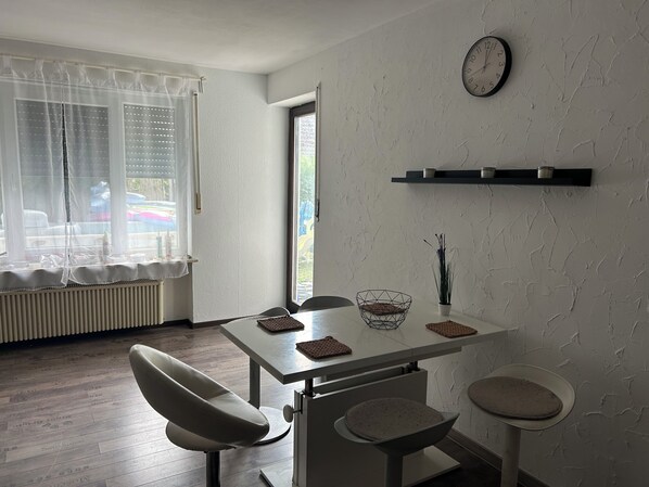 A dining area with a white table, two chairs, a clock, and a window with curtains.