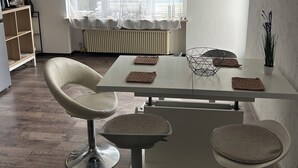 Zona pranzo moderna con tavolo bianco, due sedie imbottite e un termosifone.