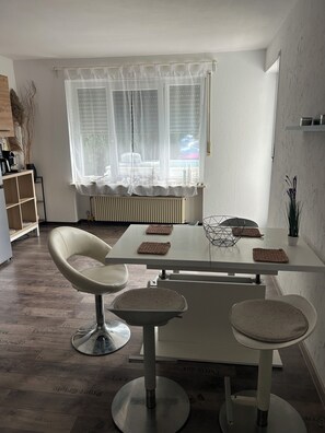 A modern dining area with a white table, two cushioned chairs, and a radiator. - Vacation rental in a quiet location, ideal for families, cyclists, and technicians (Oberaurach)