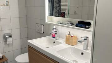 Un baño con lavamanos blanco, tocador de madera, un espejo, inodoro y perchero para toallas.