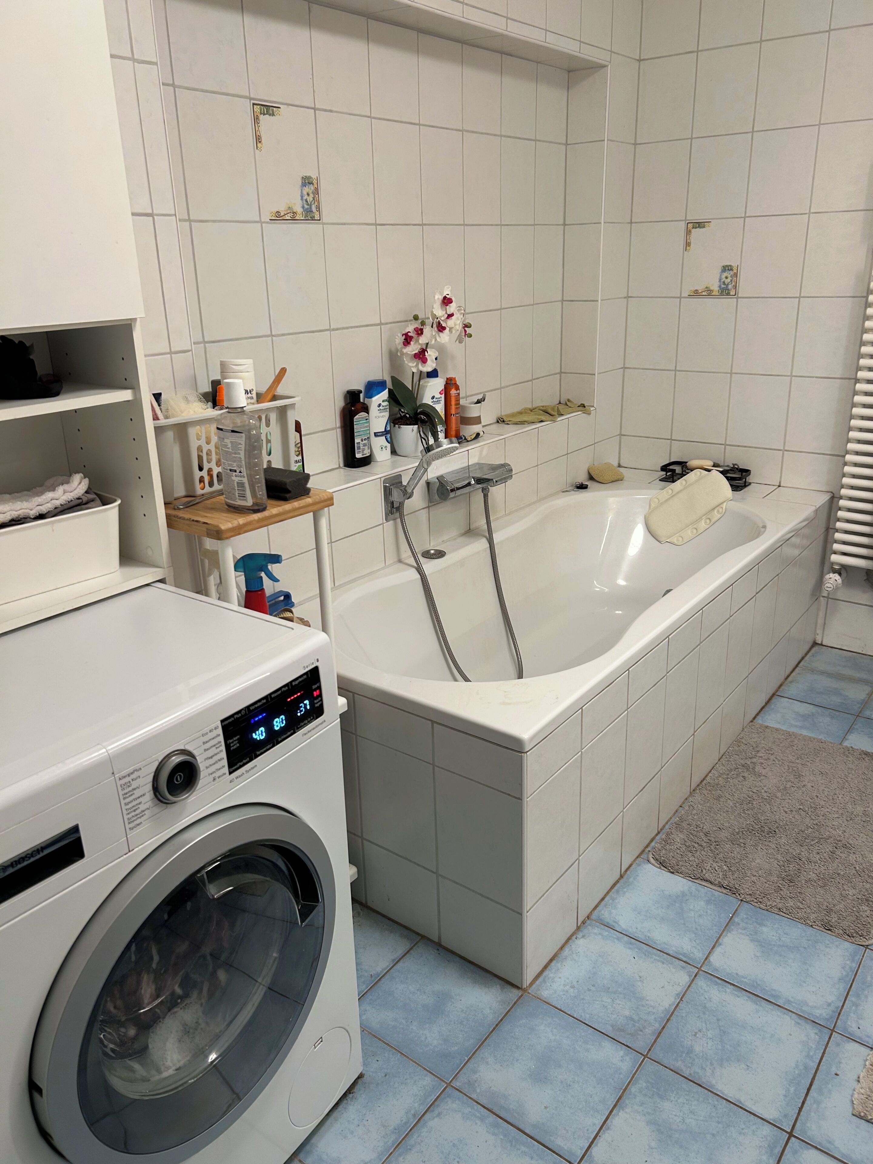 Een badkamer met een wasmachine, een bad en een plank met toiletartikelen.