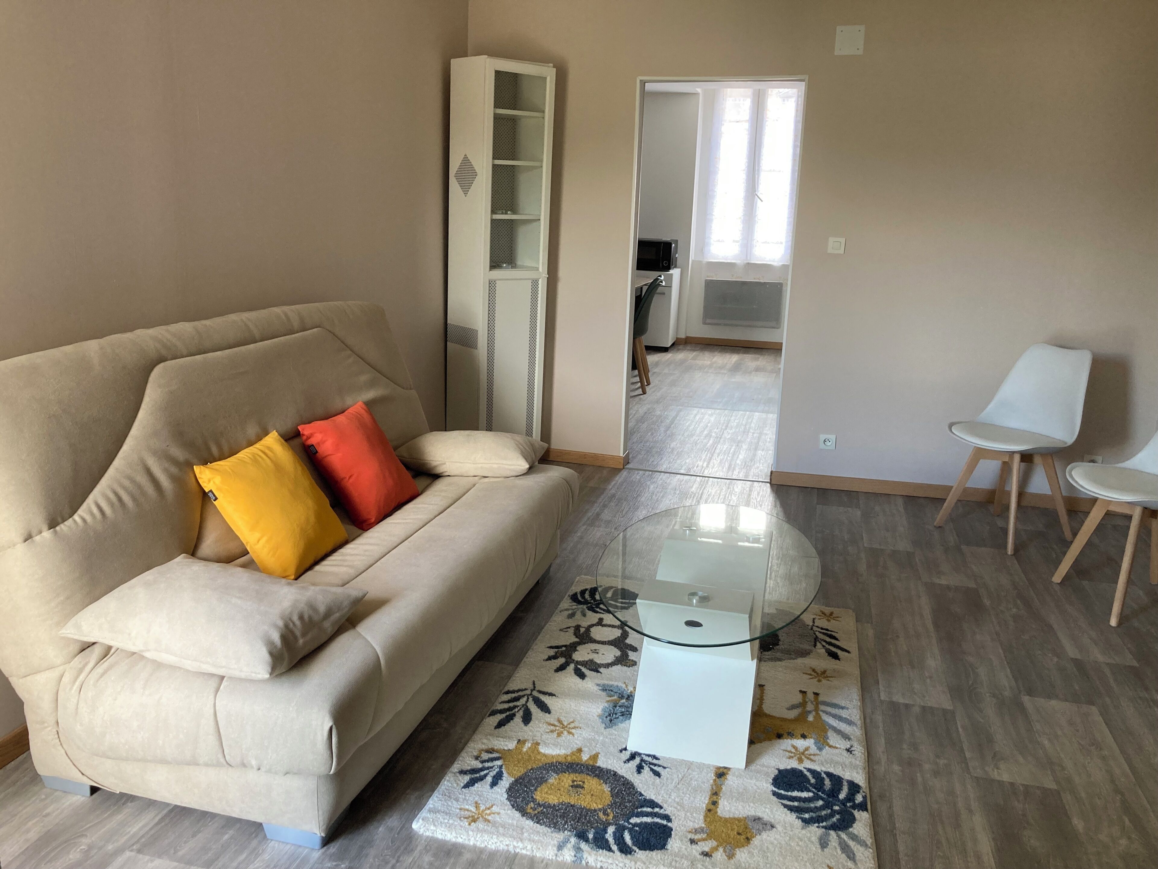 A living room with a sofa, a glass coffee table, a patterned rug, and a dining area with chairs.