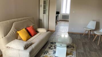 A living room with a sofa, a glass coffee table, a patterned rug, and a dining area with chairs.