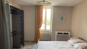 Ein Schlafzimmer mit einem Bett, einem Kleiderschrank, einem kleinen Nachttisch und einem Fenster mit Vorhängen.