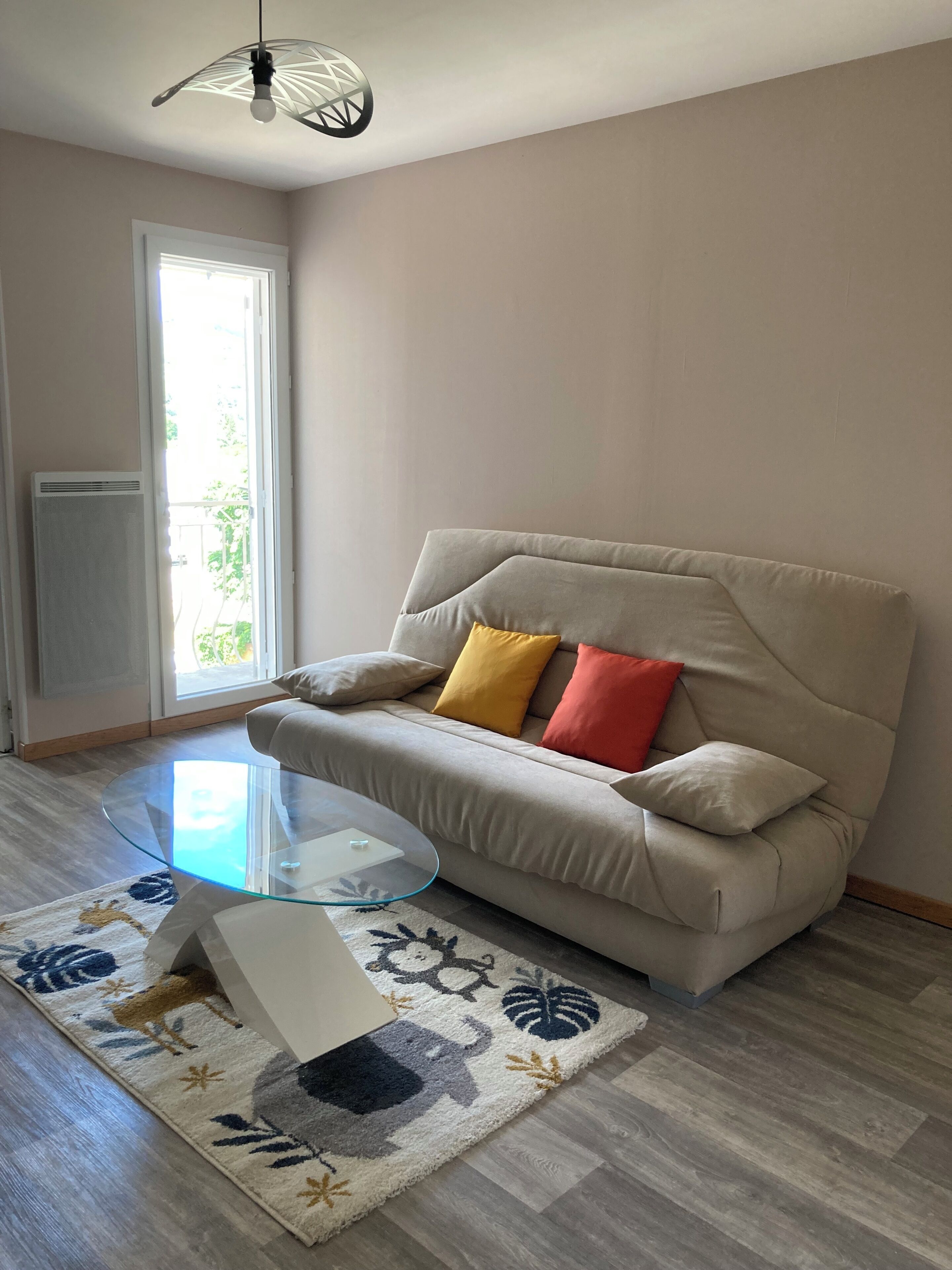 Un salon avec un canapé beige, une table basse en verre, un tapis à motifs et un luminaire suspendu au plafond.
