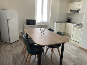Angolo cottura attrezzato con microonde, frigorifero e zona pranzo con sedie e tavolo.