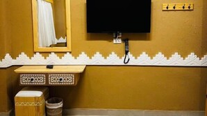 A hotel room with a bed, a television mounted on the wall, a mirror, a small wooden cabinet, and a trash bin. - Happy Oasis Hotel (Siwa)