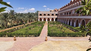 A courtyard with a central pathway leading to a building with arched windows and a tiled roof. - Happy Oasis Hotel (Siwa)
