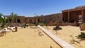 A courtyard with outdoor seating, a pathway, and a building with a traditional design. - Happy Oasis Hotel (Siwa)