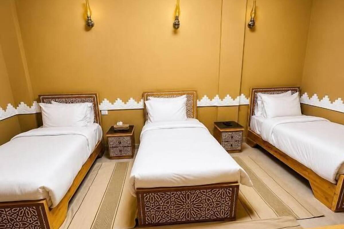 A hotel room with two beds, a wooden nightstand, a wooden desk, and a wall-mounted lamp.