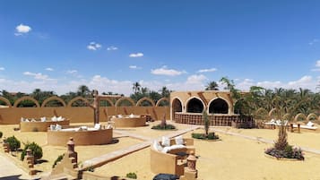 Un resort nel deserto con zone salotto all'aperto, palme e un edificio ad archi.