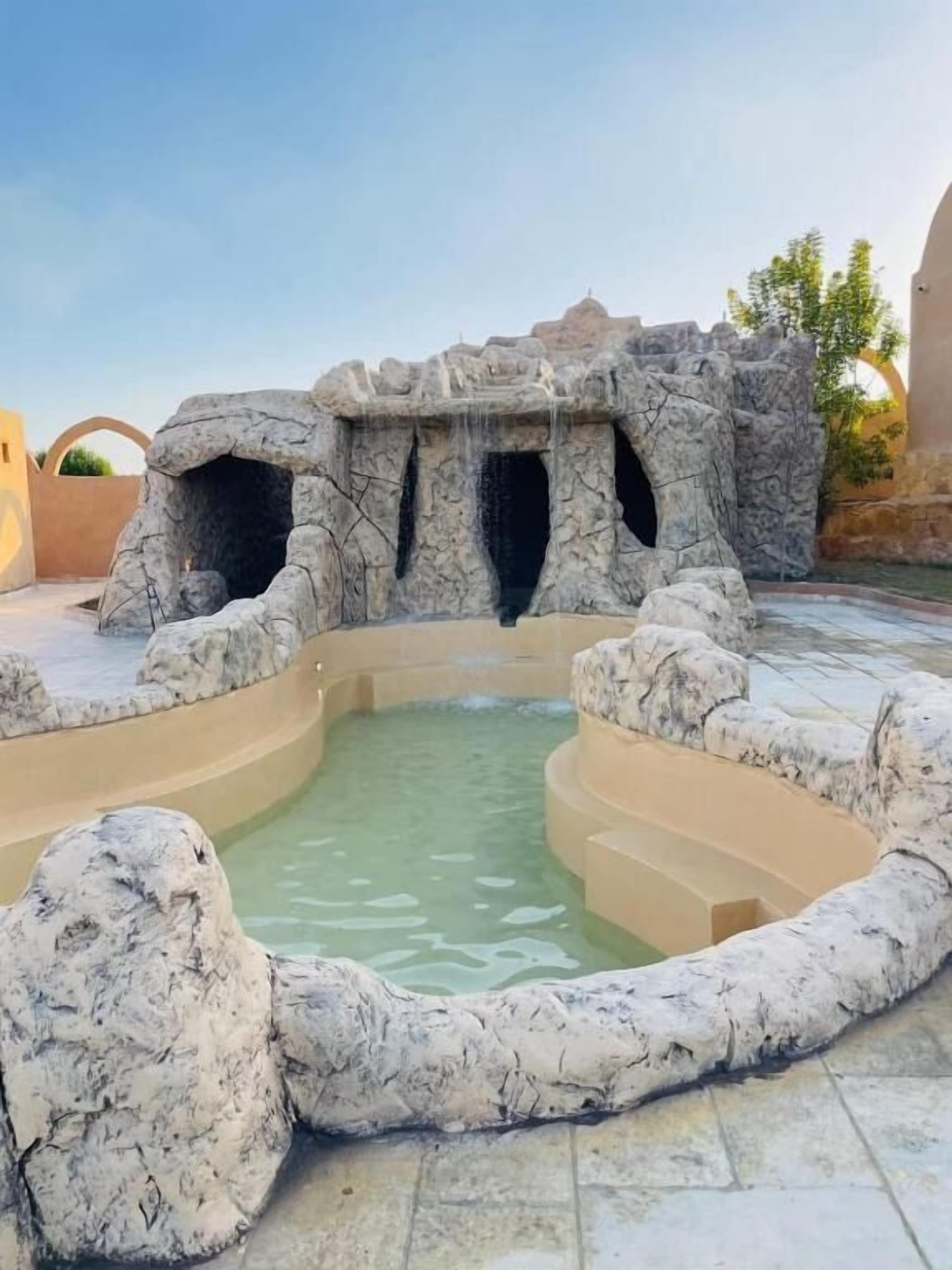 Un área de spa con una formación rocosa, una piscina y un sendero de piedra.