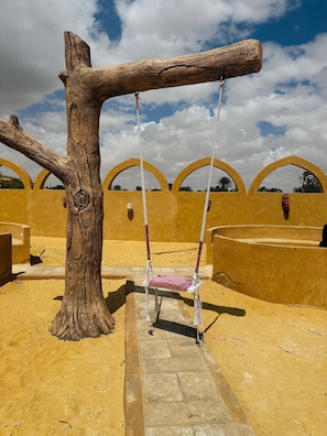 Un conjunto de columpios con forma de árbol en un área exterior con arena y cielo despejado.
