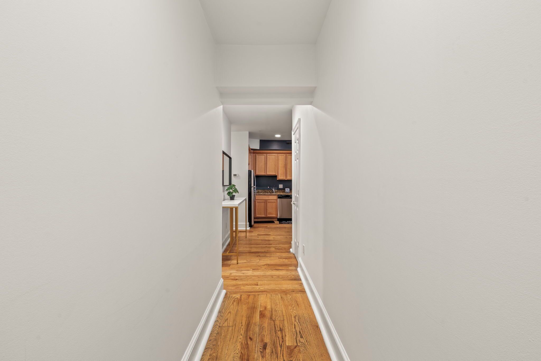 A narrow hallway with wooden flooring leading to a kitchen area with wooden cabinets and a countertop.