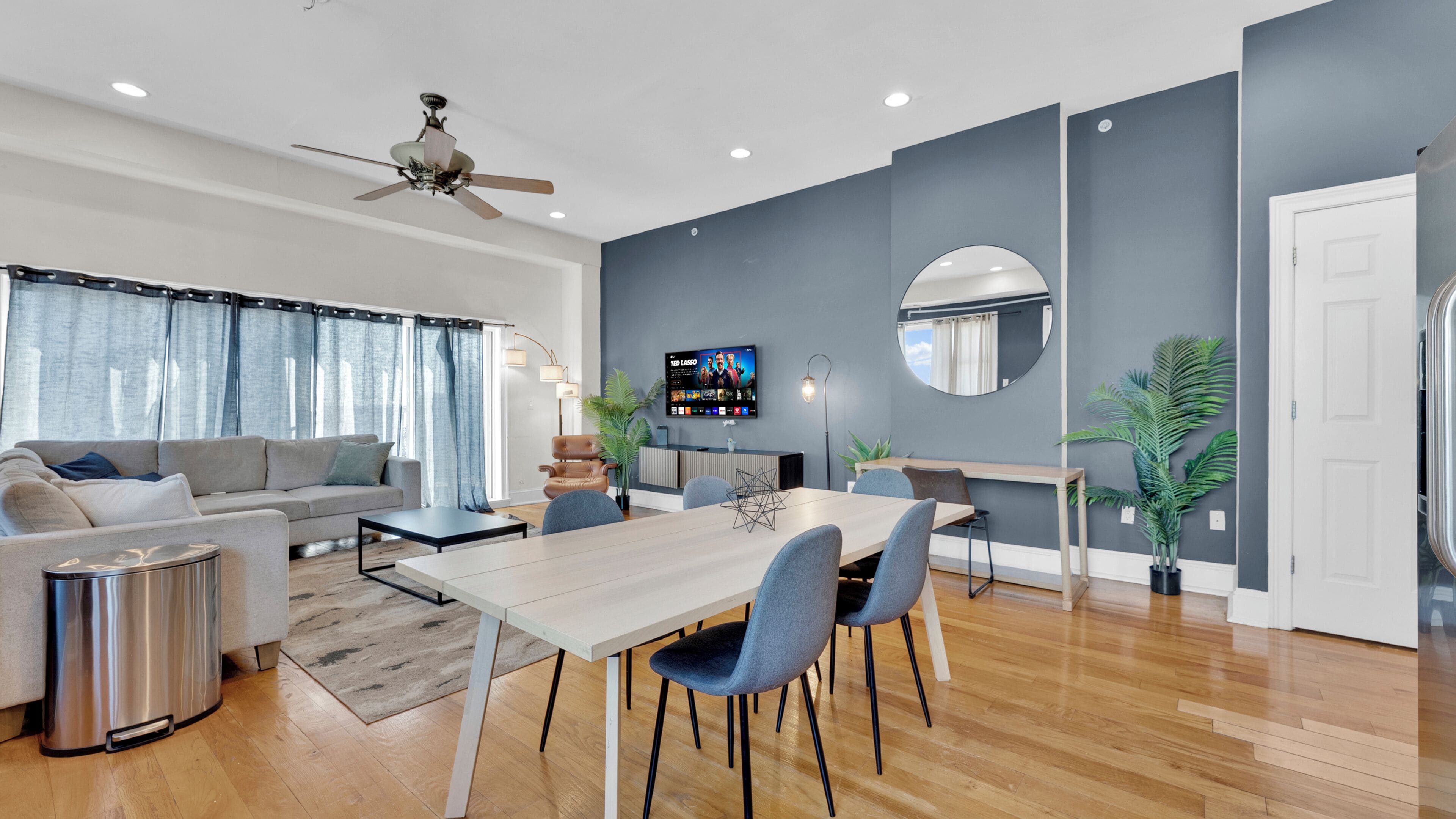 Uma sala de estar moderna com sofá, mesa de jantar, cadeiras, televisão e ventoinha de teto.