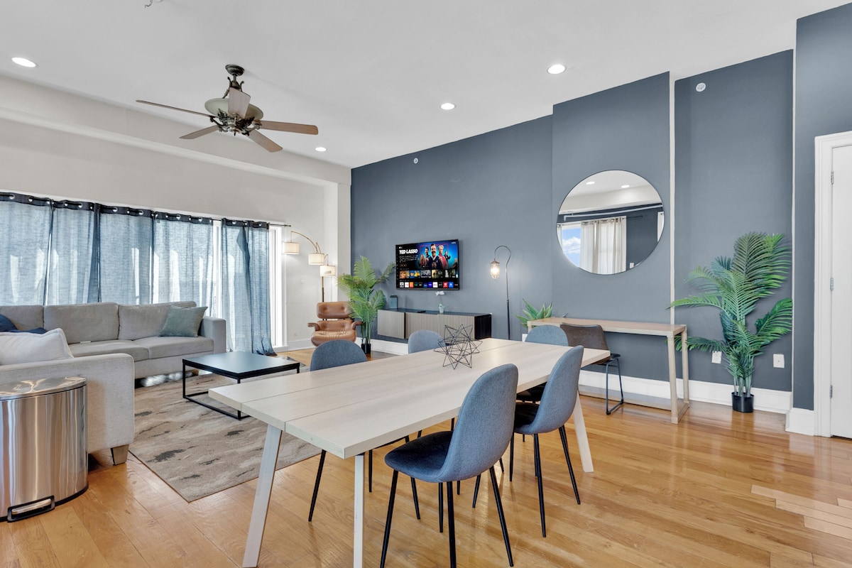 Una sala moderna con sofá, mesa de comedor, sillas, televisor y ventilador de techo.
