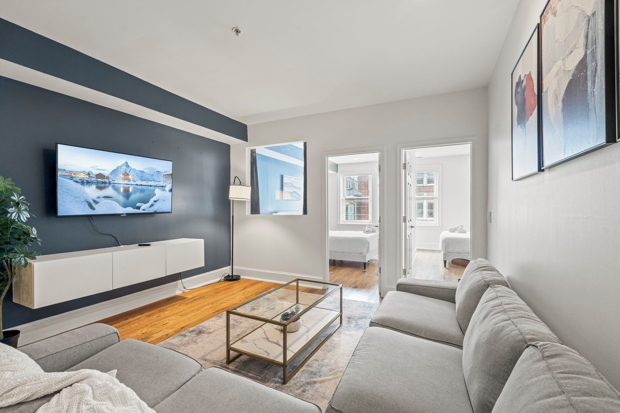 Ein modernes Wohnzimmer mit einem Flachbildfernseher, grauen Sofas, einem Couchtisch und Blick auf eine verschneite Landschaft durch das Fenster.