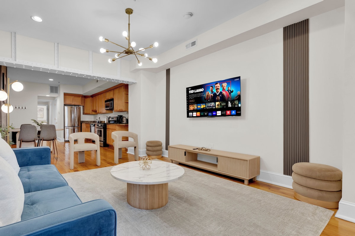 Una sala de estar moderna con un sofá azul, una mesa de centro redonda y un televisor montado en la pared.