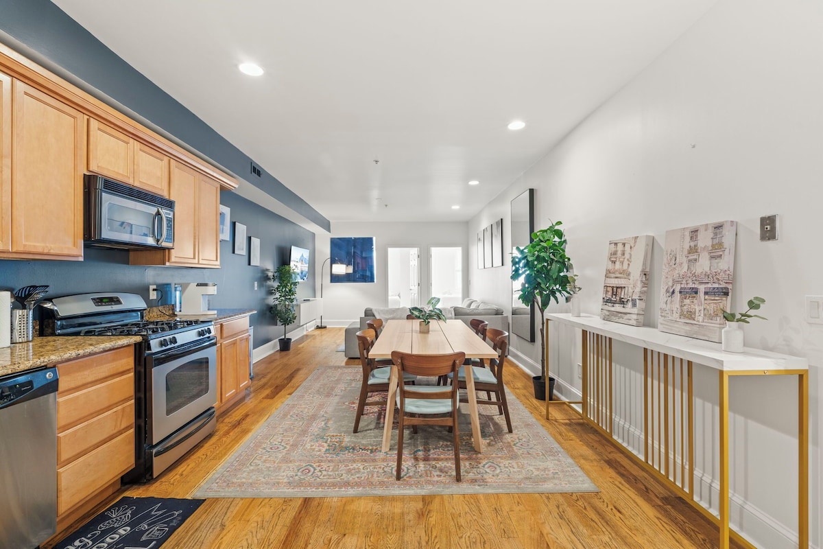 Una cocina moderna con armarios de madera, electrodomésticos de acero inoxidable y un comedor con mesa y sillas de madera.