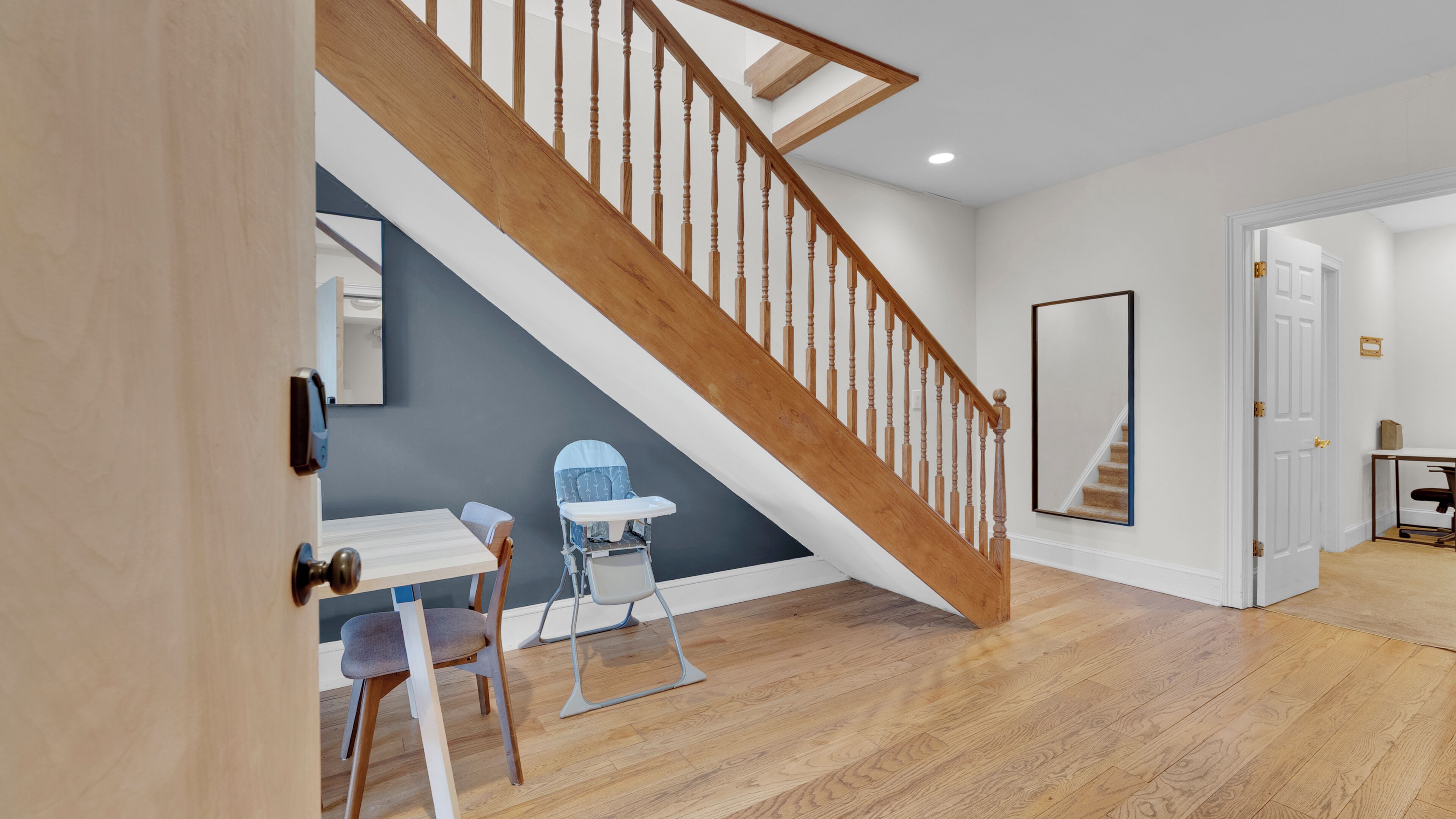 Un escalier avec des balustrades en bois, une porte blanche, un miroir et une petite table avec une chaise.