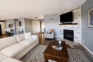 Ein Wohnzimmer mit einer Couch, einem Couchtisch, einem gemusterten Teppich, einem Kamin und einem an der Wand montierten Fernseher.