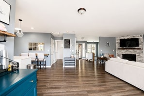 A modern living room with a fireplace, a kitchen area with bar stools, and a dining area with a chandelier. - Sound View Retreat Near Illahee Beach & Ferry (Bremerton)