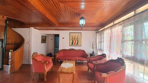 A room with a wooden ceiling, a staircase, a sofa set, a table, and a painting on the wall. - Cozzy Villa Swasti Cisarua (bogor)