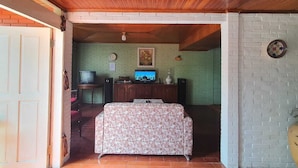An open-plan living area with a wooden ceiling, a television, a floral sofa, and a brick wall. - Cozzy Villa Swasti Cisarua (bogor)