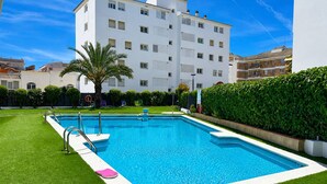 A rectangular swimming pool with a white border, surrounded by artificial green grass, and a palm tree in the foreground. - Sitges Oasis Apartment with Balcony (Sitges)