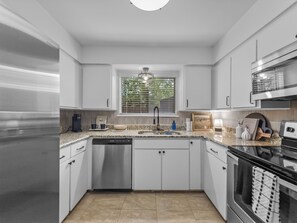 Een moderne keuken met witte kasten, roestvrijstalen apparatuur, een vaatwasser en een raam met zonwering.