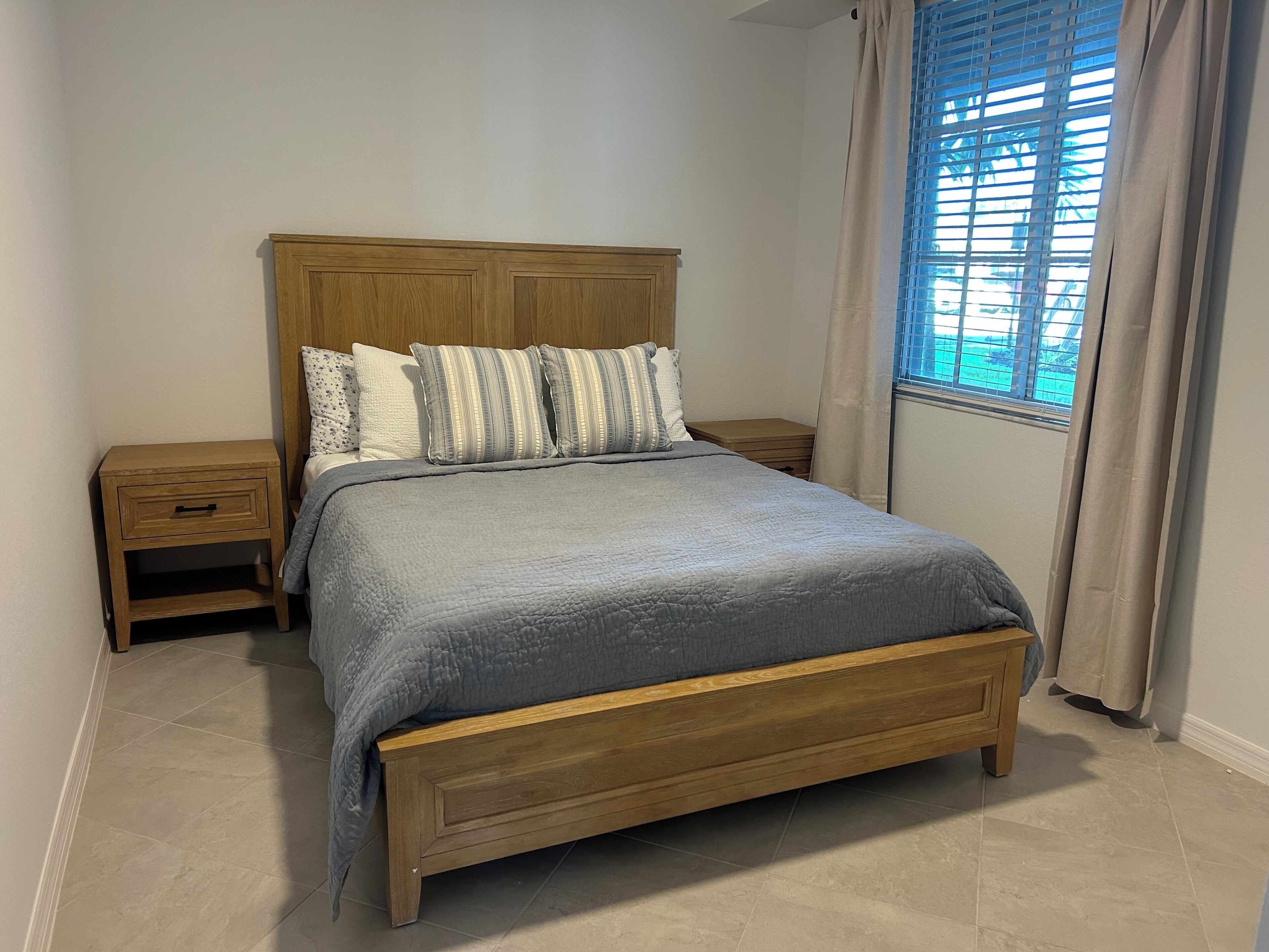 A bedroom with a wooden bed, a nightstand, a bedside table, and a window with curtains.