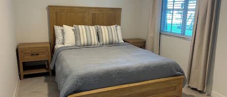 A bedroom with a wooden bed, a nightstand, a bedside table, and a window with curtains.