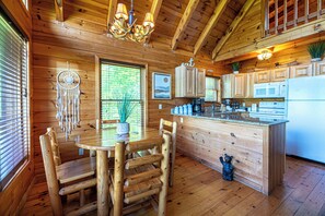 A wooden cabin interior with a dining table, chairs, a kitchen with cabinets and appliances, and a bear decoration. - Chic Boho~Private Mtn View Cabin~Hottub & 2 Kings (Sevierville)