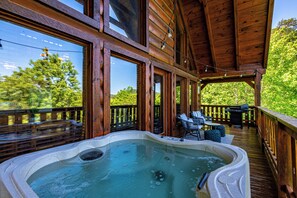 Un jacuzzi en una terraza de madera con amplios ventanales y vista a árboles.
