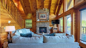 Een chalet inrichting met een stenen openhaard, een bank met kussens, een televisie en houten wanden.