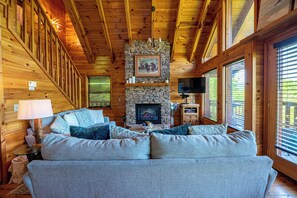 A log cabin interior with a stone fireplace, a sofa with cushions, a television, and wooden walls. - Chic Boho~Private Mtn View Cabin~Hottub & 2 Kings (Sevierville)