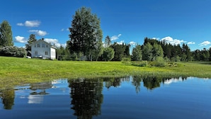 Una casa con un jardín grande y un estanque que refleja el cielo.