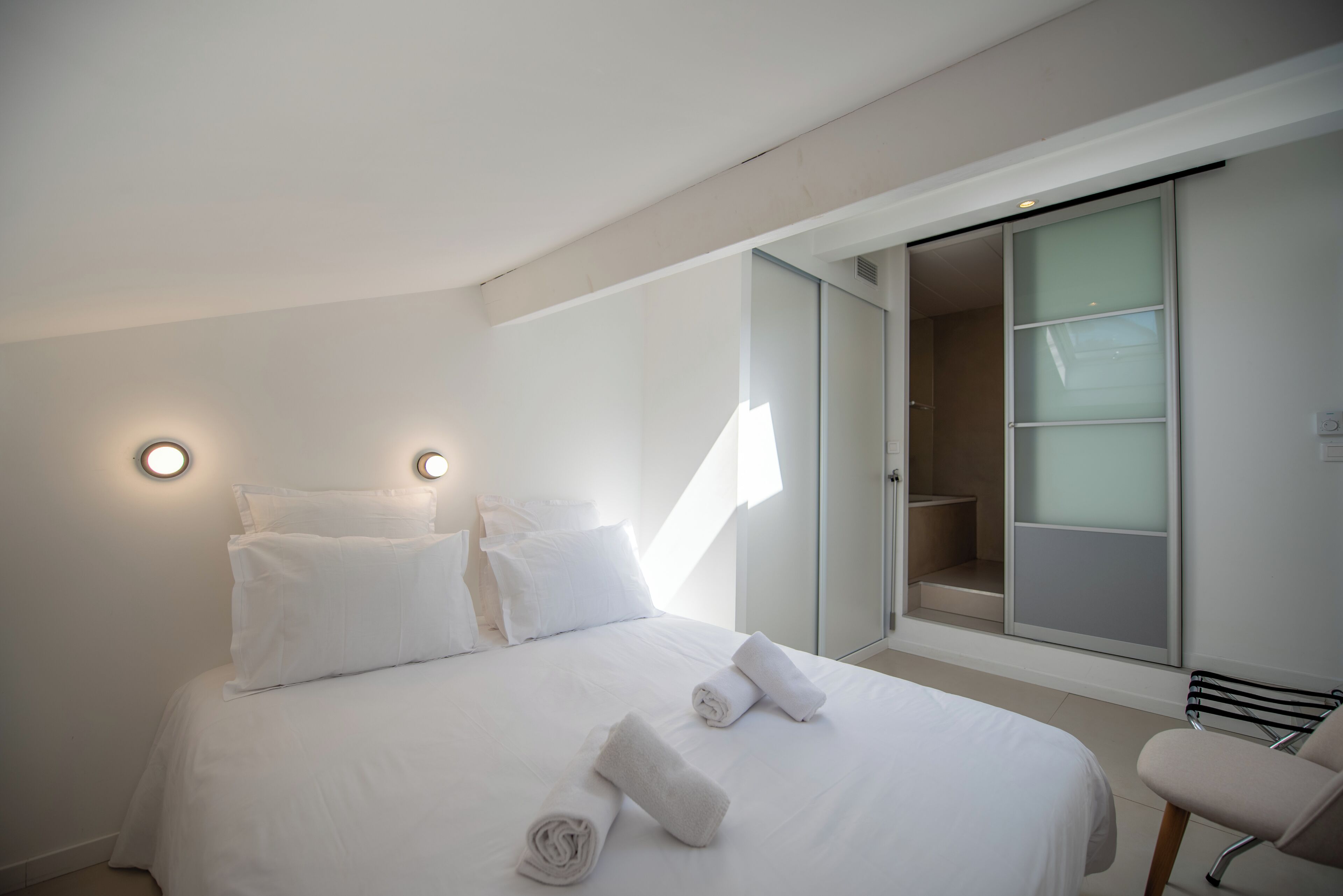 A hotel room with a large bed, two bedside lamps, a wardrobe, and a chair.