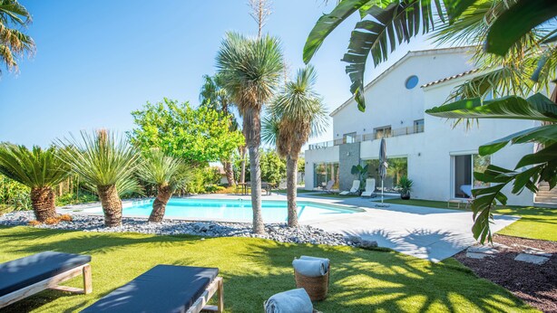 Un área junto a la piscina con sillones de descanso, una piscina y un edificio moderno de color blanco.