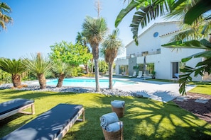 A poolside area with lounge chairs, a swimming pool, and a white building with a modern design. - Villa Joia 2 Saint Tropez (Gassin)