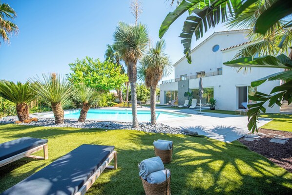 A poolside area with lounge chairs, a swimming pool, and a white building with a modern design.