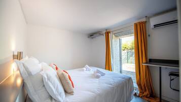 A hotel room with a bed, a desk, an air conditioning unit, and a view through the window.