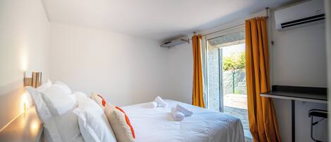 A hotel room with a bed, a desk, an air conditioning unit, and a view through the window.