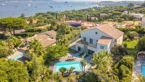 Una propiedad costera con piscina, una casa grande con tejado de tejas y vista al mar con barcos.