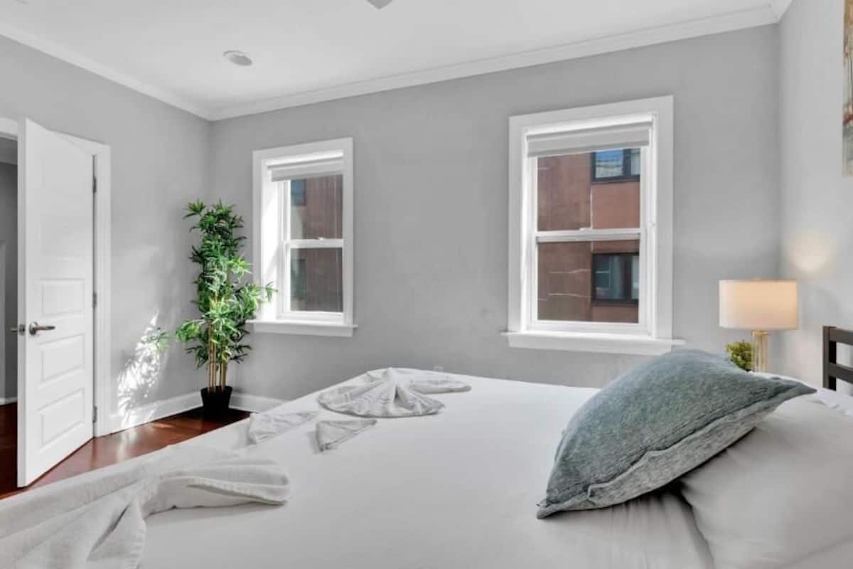 A bedroom with a bed, a potted plant, a lamp, and a view of the outside.