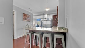 Una cocina con barra, taburetes, una lámpara colgante y un cuadro en la pared.