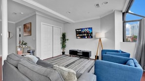 A modern living room with a grey sofa, blue armchairs, a black entertainment unit, and a TV displaying a movie. - Apartmint at 602 2nd St Philadelphia (Philadelphia)