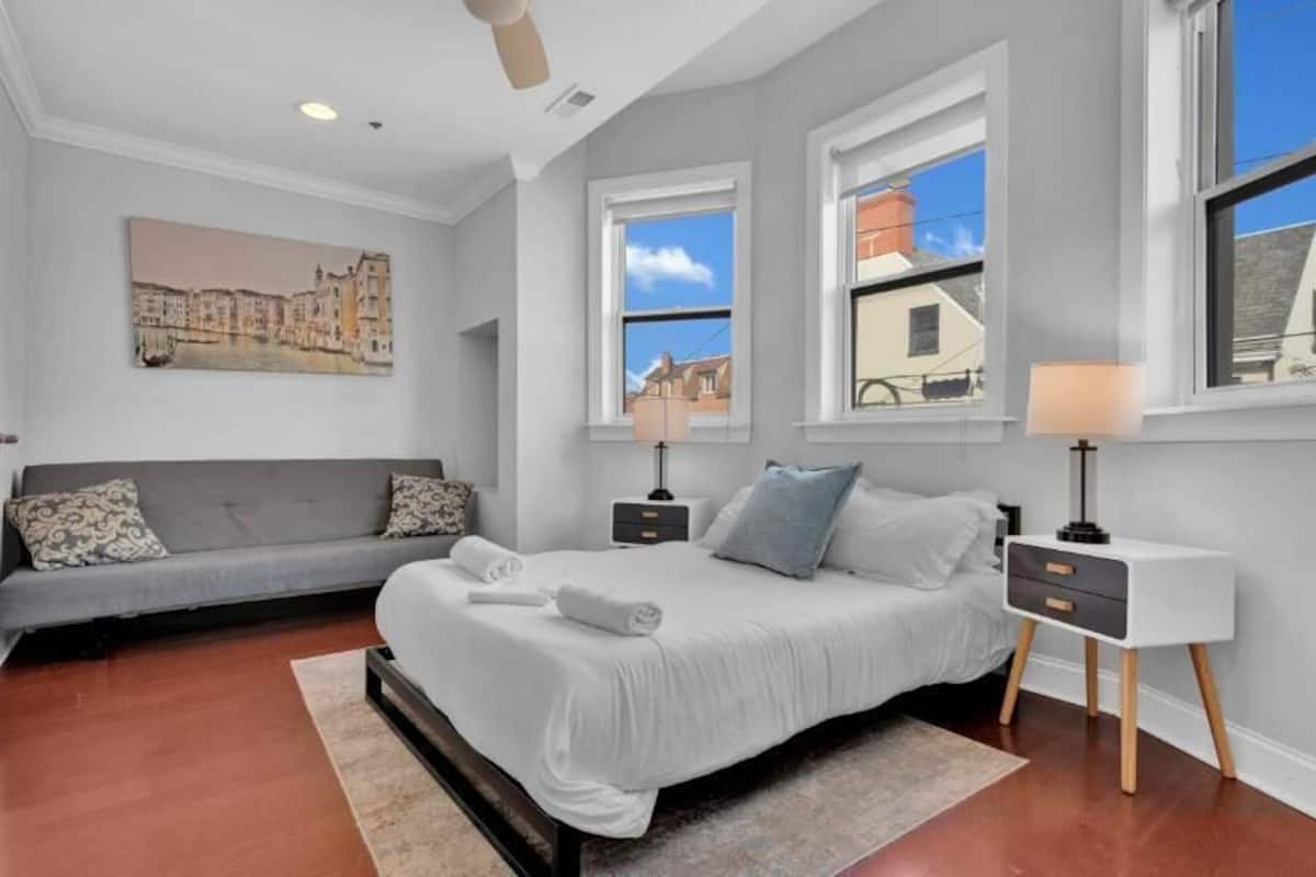 A bedroom with a bed, a sofa, a nightstand, a lamp, and a painting on the wall.